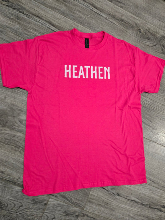 Pink t-shirt with 'HEATHEN' printed on it laid flat on a wooden floor.