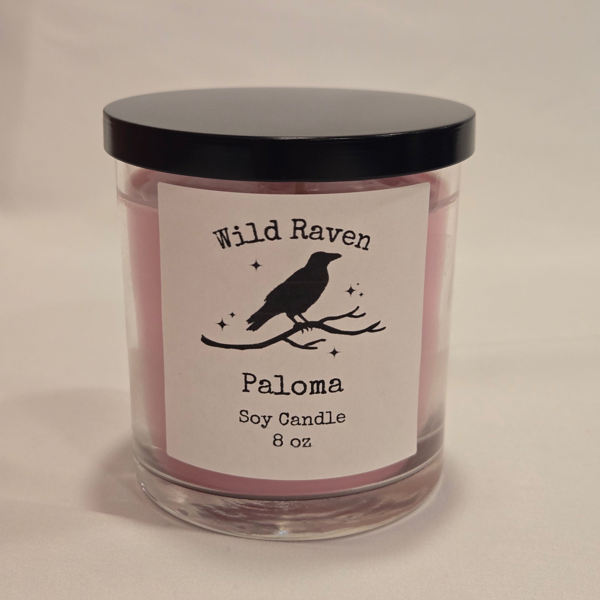 A 8 oz soy candle in a clear glass jar with a black lid and a white label featuring a black raven silhouette and the brand name Wild Raven.